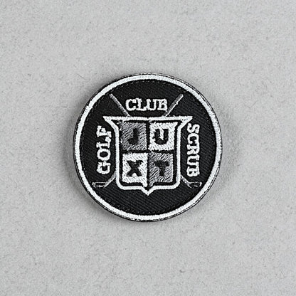 JUXT Golf Co. black circular patch with white and grey embroidery. Features crossed golf clubs and a shield with 'JU' and 'XT' inside.